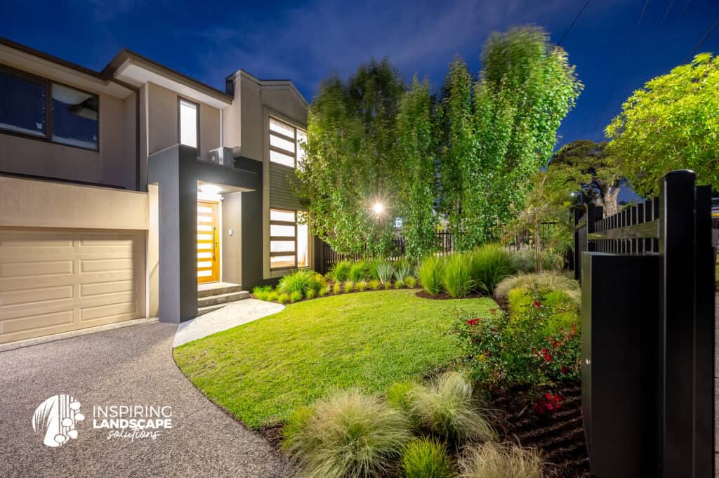 View of the frontyard and the front facade of the house from the driveway, lit up by lights.